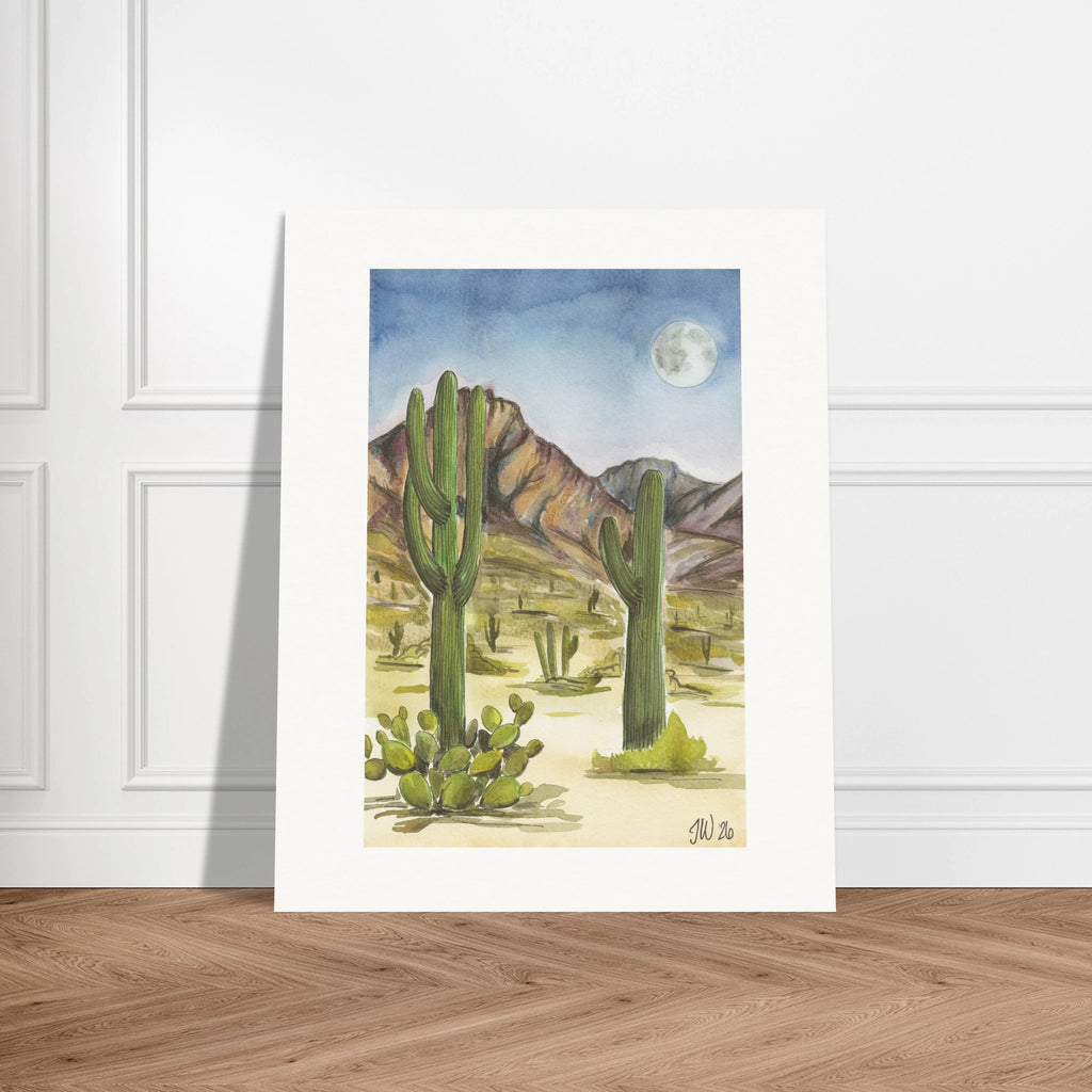 Fine art print by Houston based artist Jenny Wagner, Desert Moon. This watercolor print depicts a desert scene with saguaro cacti and a full moon in the background. Print shown leaning against a neutral wall
