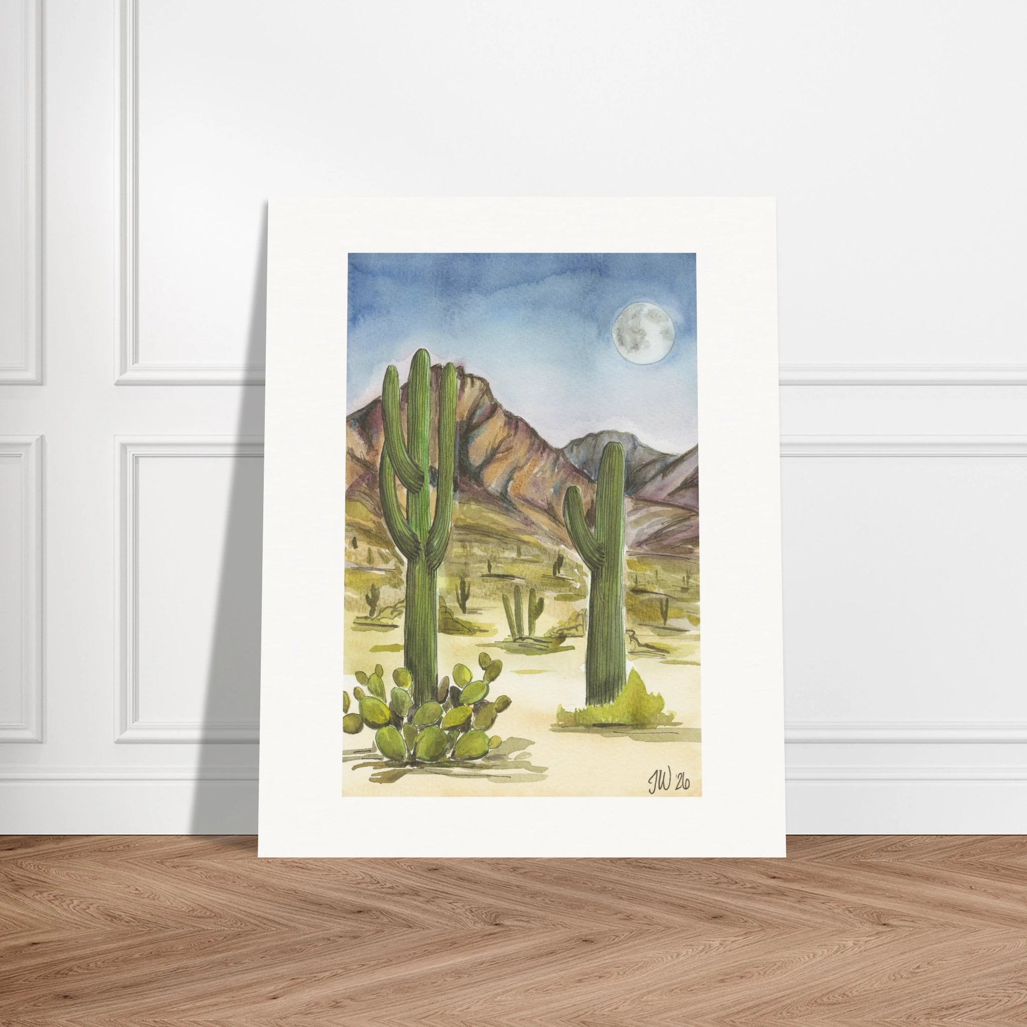 Fine art print by Houston based artist Jenny Wagner, Desert Moon. This watercolor print depicts a desert scene with saguaro cacti and a full moon in the background. Print shown leaning against a neutral wall