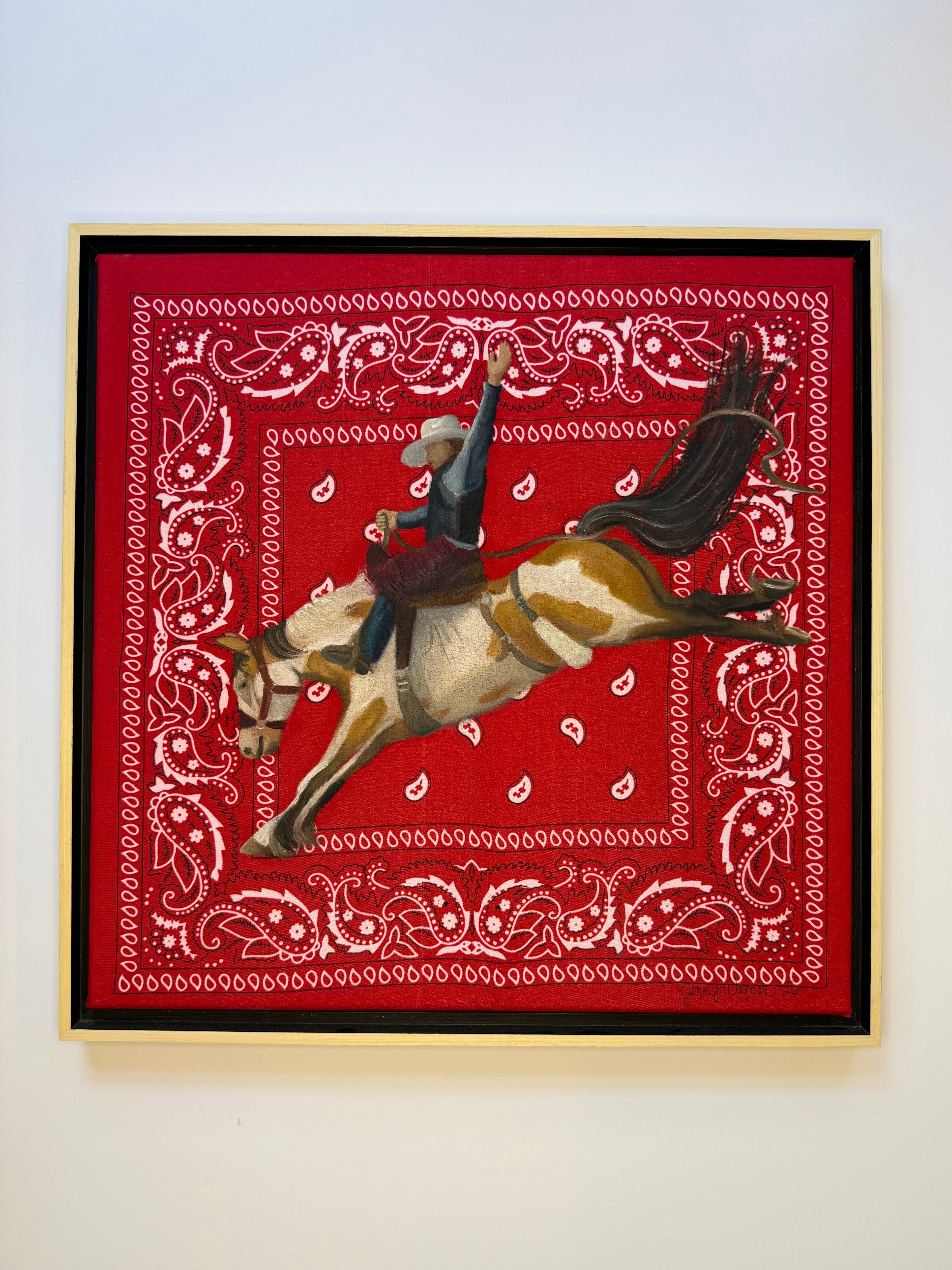 Hold On painting by Texas artist Jenny Wagner shown in its frame, a bronc rider is shown mid buck and painted on a red bandana