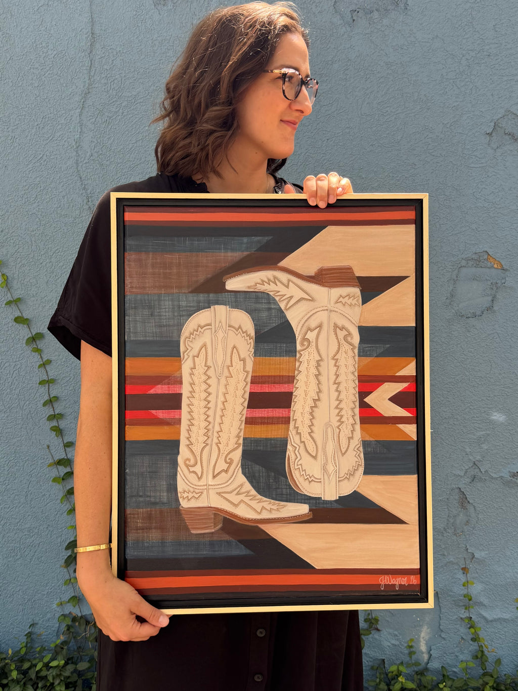 Original acrylic painting, Paired, held by Texas artist Jenny Wagner. This painting features a pair of tall cream boots in front of a southwestern patterned background. This 18x24 painting is framed in a natural wood floater frame.