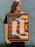 Original acrylic painting, Paired, held by Texas artist Jenny Wagner. This painting features a pair of tall cream boots in front of a southwestern patterned background. This 18x24 painting is framed in a natural wood floater frame.