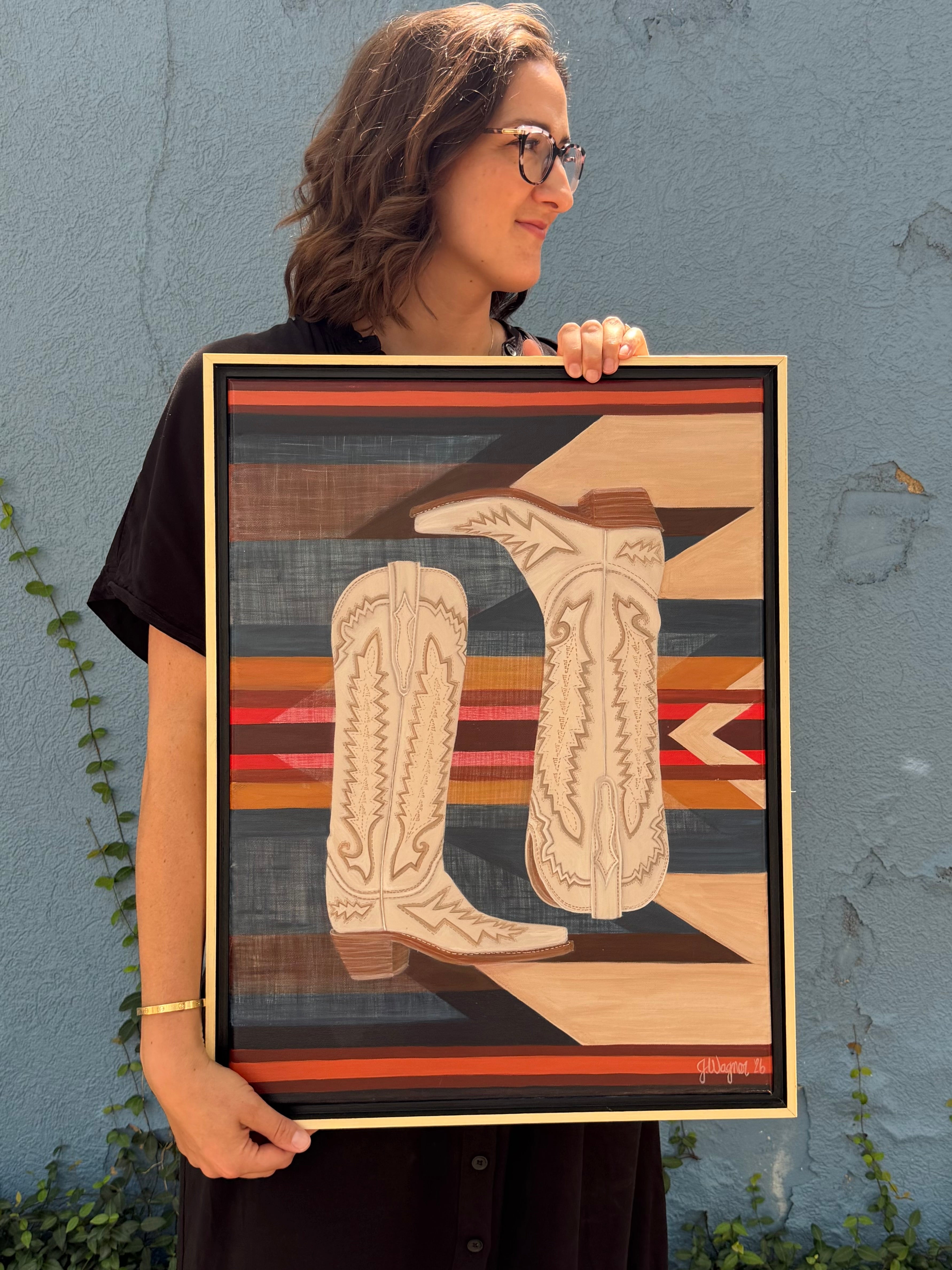 Original acrylic painting, Paired, held by Texas artist Jenny Wagner. This painting features a pair of tall cream boots in front of a southwestern patterned background. This 18x24 painting is framed in a natural wood floater frame.