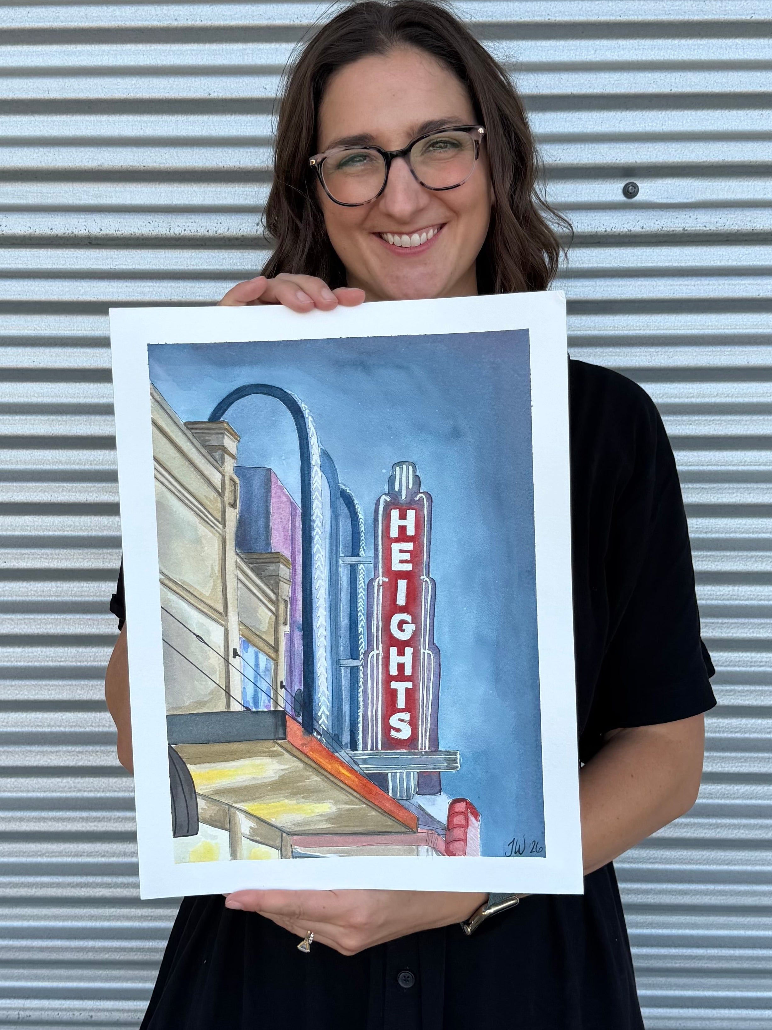 Jenny Wagner holding the original watercolor painting, "The Heights Theater" featuring Houston's iconic theater marquee