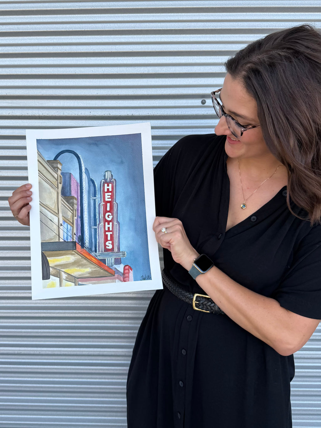 Side view of artist Jenny Wagner displaying the original watercolor painting "The Heights Theater"