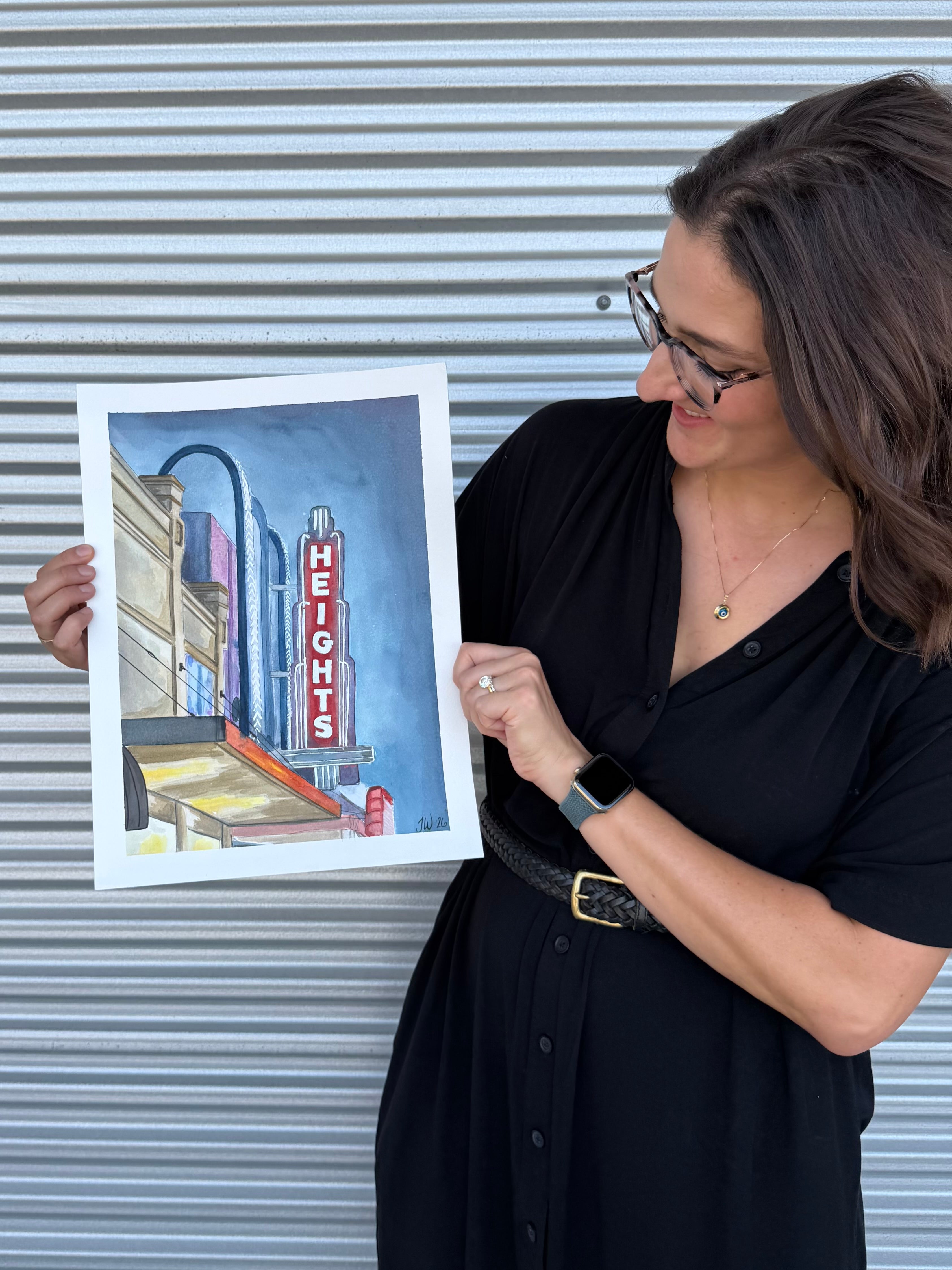 Side view of artist Jenny Wagner displaying the original watercolor painting "The Heights Theater"