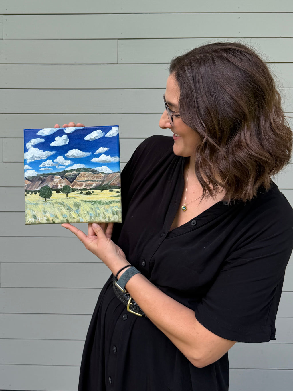 Side view of artist Jenny Wagner holding the original 10x10 acrylic landscape painting "Colorado to Utah"