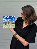Side view of artist Jenny Wagner holding the original 10x10 acrylic landscape painting "Colorado to Utah"