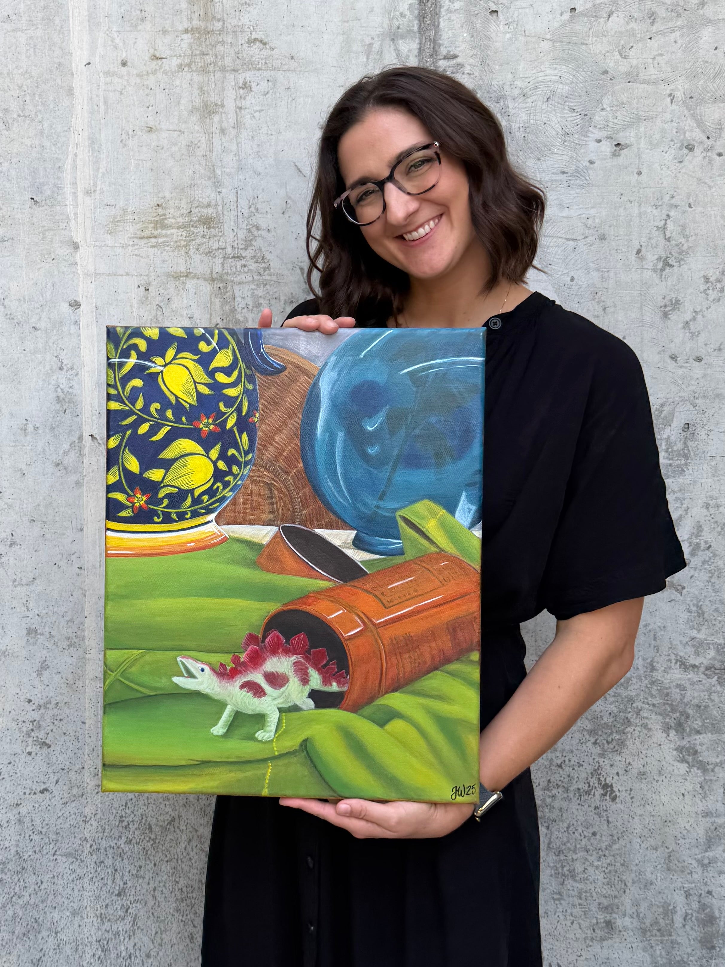 Texas artist, Jenny Wagner, holding her original acrylic still life, The Unexpected Guest. This 16x20 still life shows the usual suspects like baskets, vases, and pottery, but a surprising dinosaur figurine is also pictured.