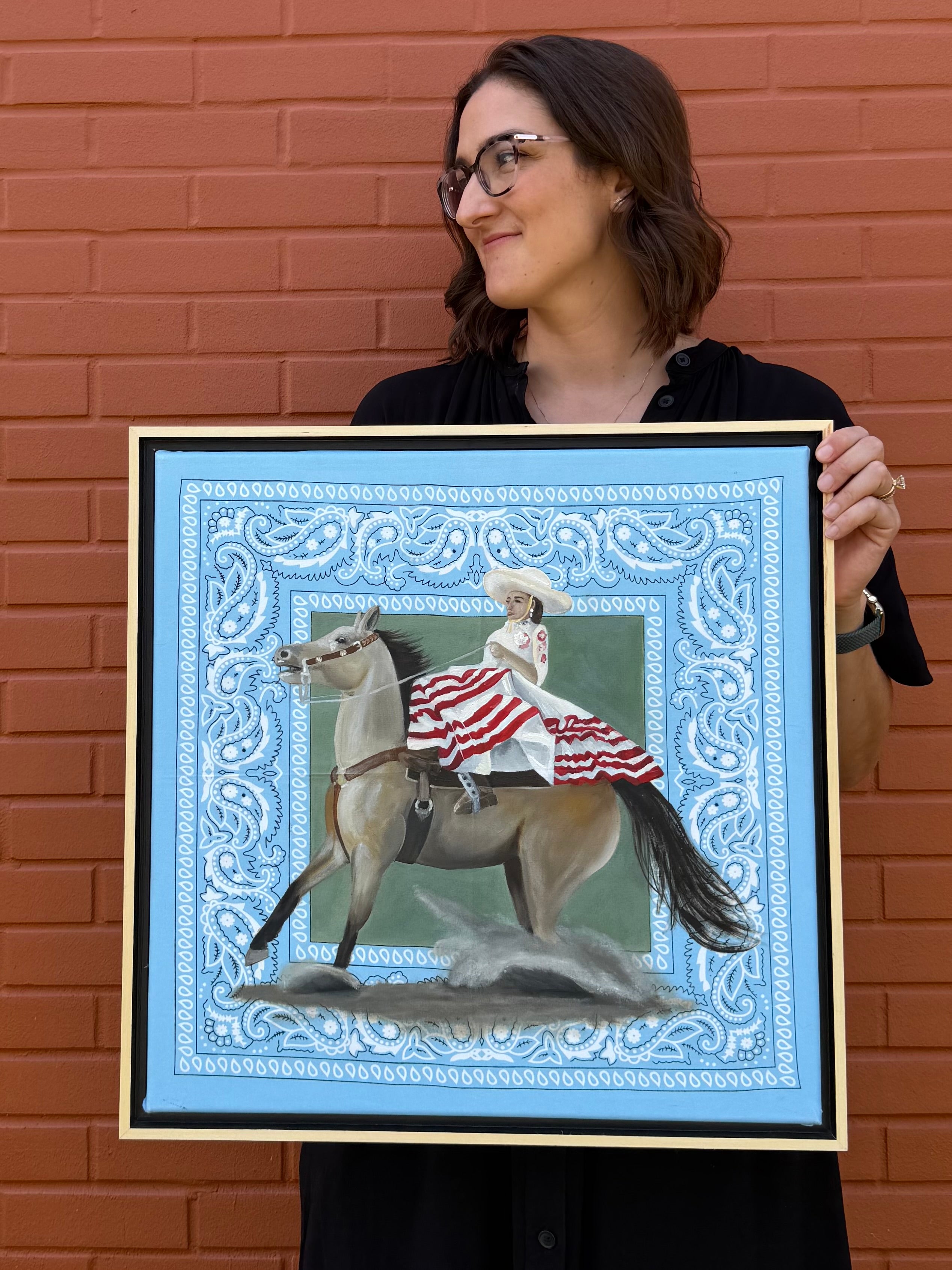 Texas artist, Jenny Wagner with her original Oil Painting, La Escaramuza. This painting features a female Escaramuza rider in traditional dress, side saddle while her horse races to a stop. Painted on a blue bandana, part of the Bandana Series
