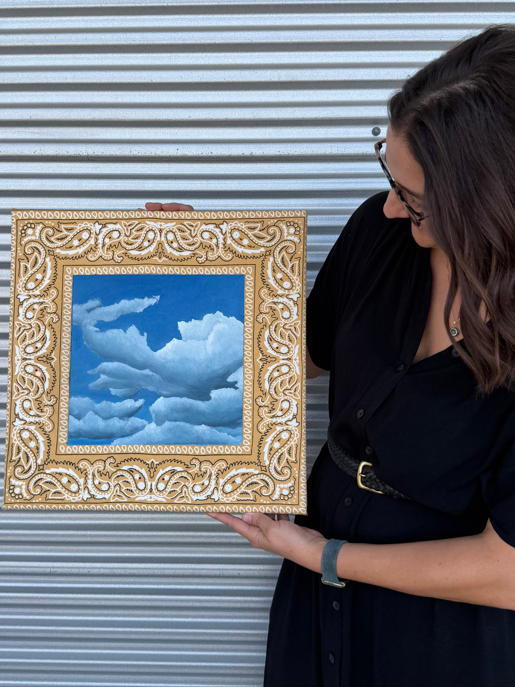Texas artist, Jenny Wagner, with her oil painting Bandana Sky. This painting is done on a golden yellow hand stretched bandana with a deep blue sky with clouds.