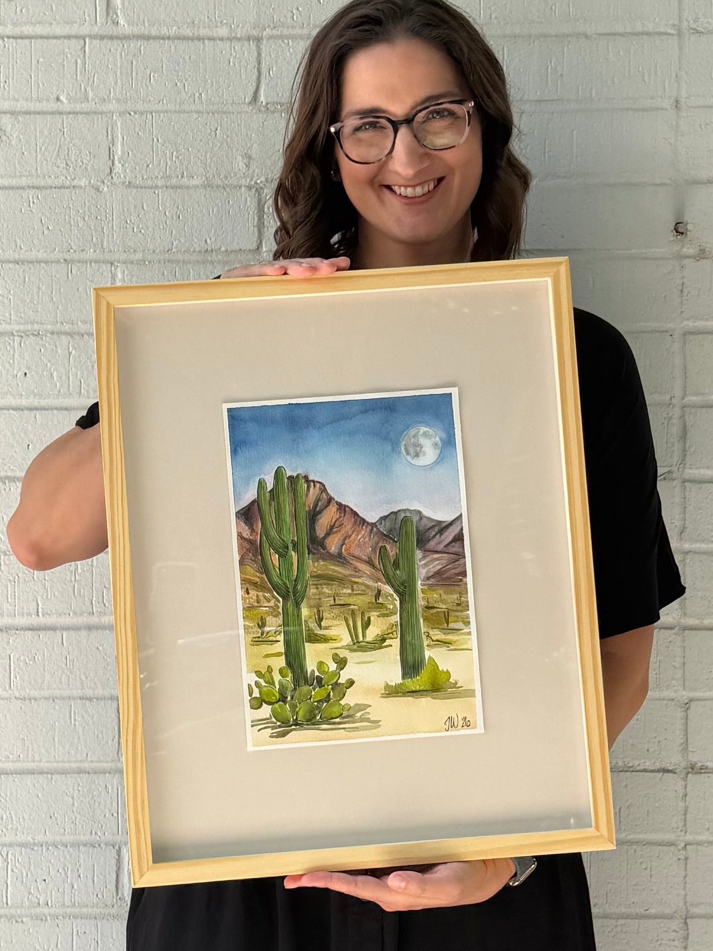 Texas artist, Jenny Wagner, shown with her original watercolor painting Desert Moon. This western watercolor landscape depicts a desert scene at night, complete with various cactus varieties, a full moon and a mountainous scene in the distance.
