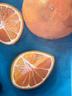 close up of Oranges on Blue, still life by Texas artist Jenny Wagner. A close-up painting of citrus fruits on a textured blue background, showing one whole orange and two orange slices with visible canvas texture.